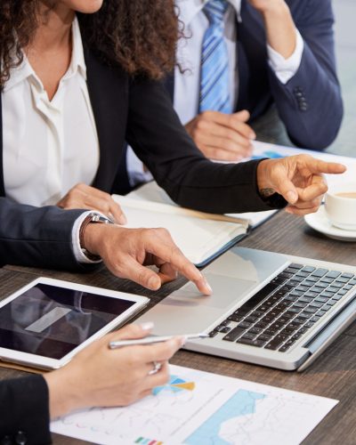 Faceless shot of coworking businesspeople surfing laptop while discussing project at table in office